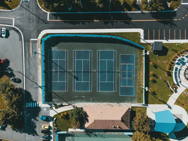 Aerial view showcasing tennis courts next to roads and parked cars in an urban setting