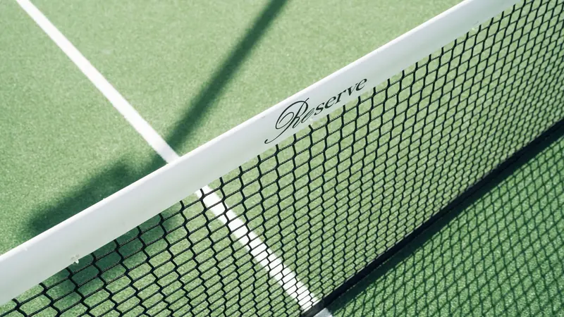 Close-up of a tennis net on a green court with 'Reserve' label casting a shadow