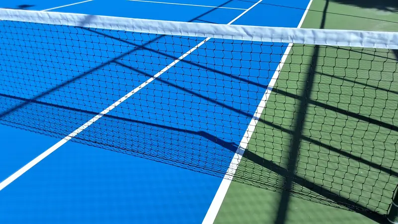 Close-up view of a tennis court with blue and green surfaces, featuring the net and shadows