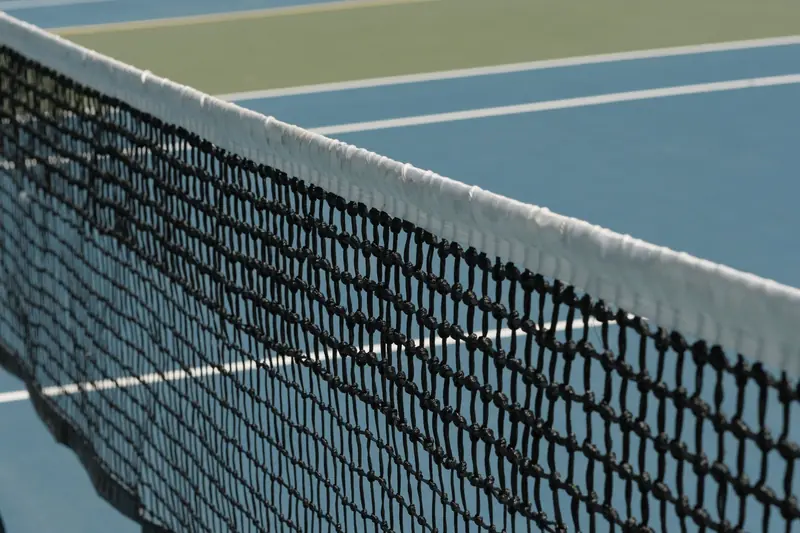 Detailed perspective of a tennis net casting shadows on a vibrant blue court under sunlight