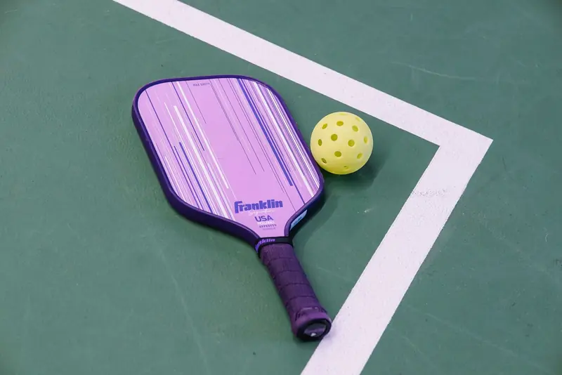 A purple pickleball paddle and yellow ball on a green court