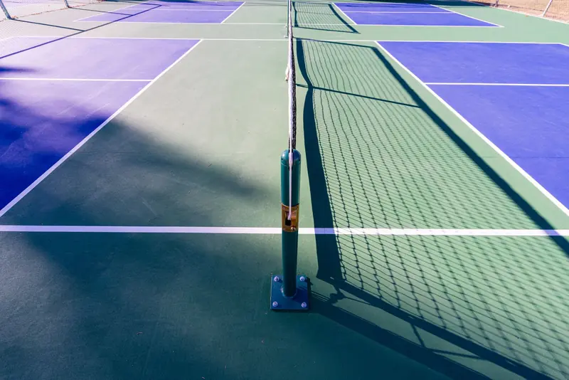 A pickleball court with blue and green surfaces under sunlight, showcasing the net and court lines