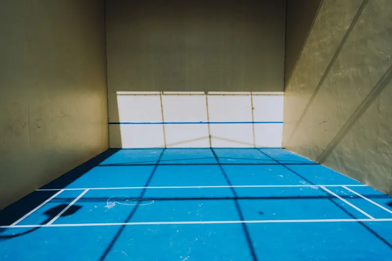 A pickleball court illuminated by sunlight, creating unique shadow patterns on the blue floor