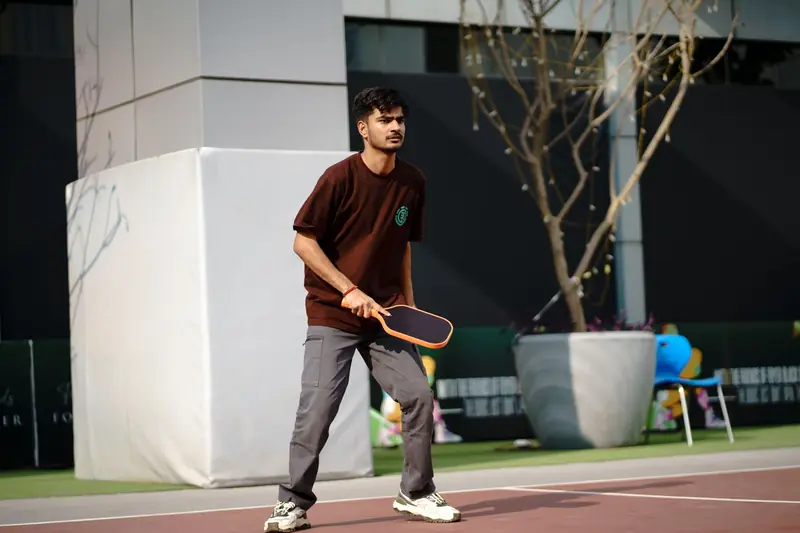 A young man actively playing pickleball on an outdoor court, showcasing concentration and skill