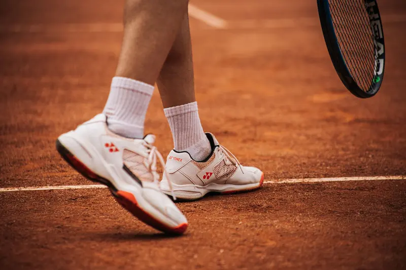 Close-up of a tennis player on a clay court preparing to serve with racket and shoes